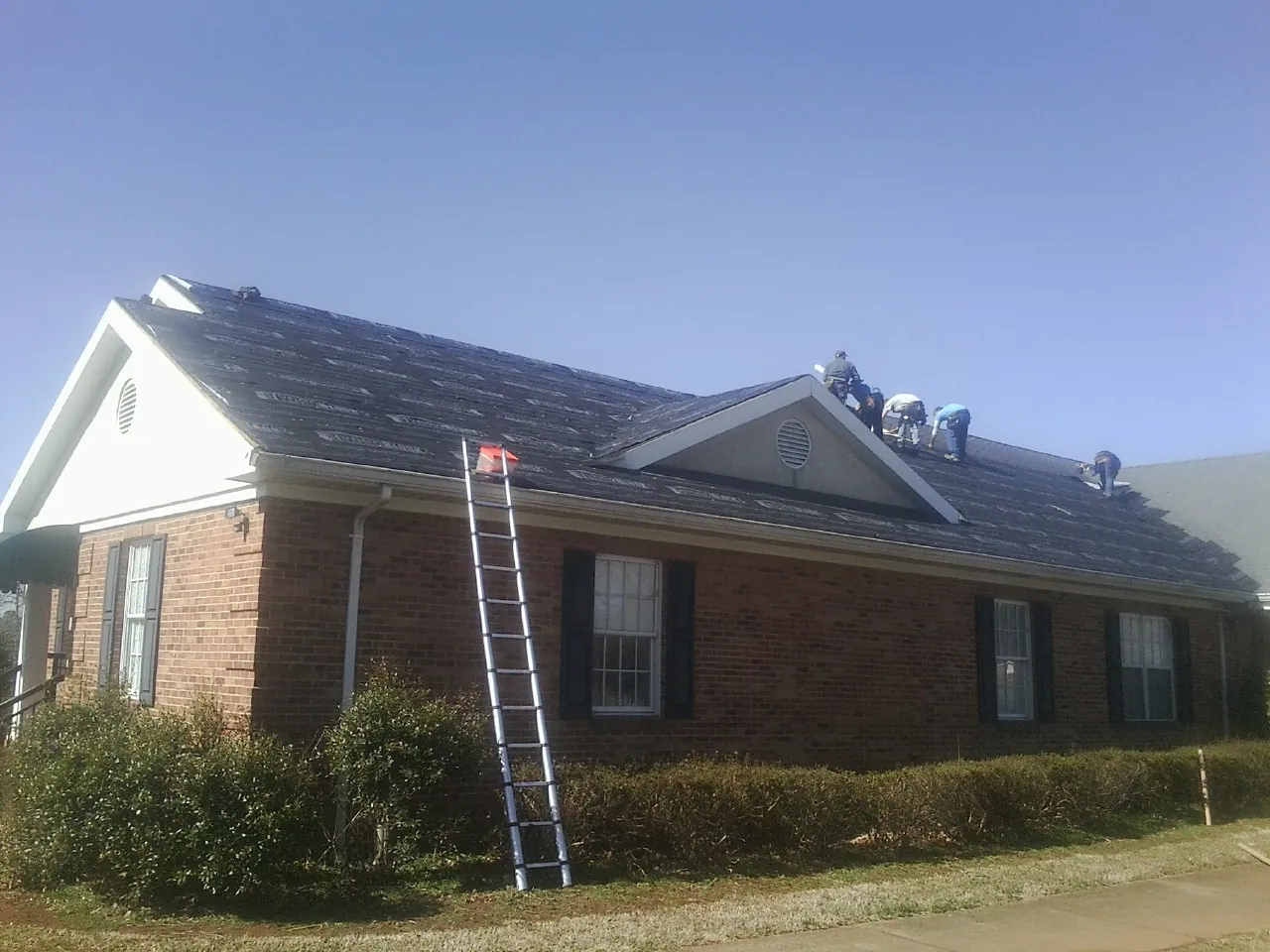 Crew tearing shingles off a brick ranch roof with a ladder set — Metal Roof Repair work by our crew in Ridgely