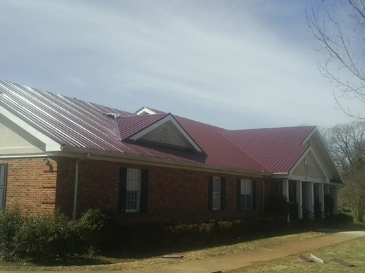 Red metal roof with gabled entries on a long brick building, from a Hail Damage Roof Repair job in Ridgely