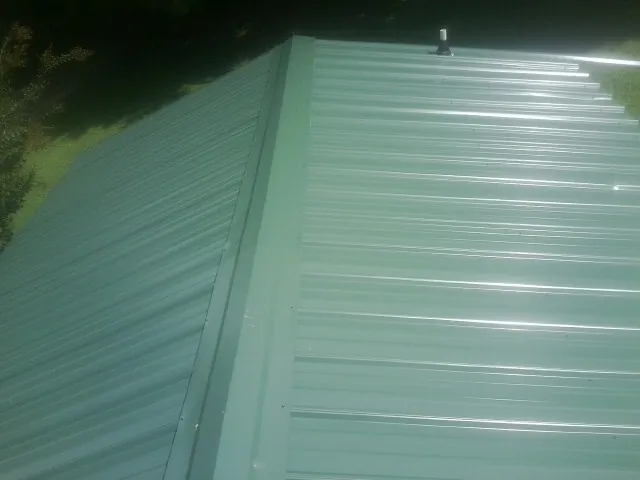 New green metal panels meeting at the ridge of a roof — Flat Roof Repair work by our crew in Ridgely
