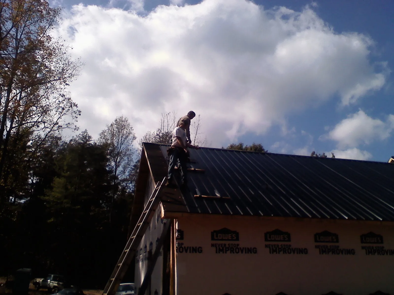 Roofer fastening dark metal panels high against a cloudy sky, from a Roof Inspection job in Ridgely