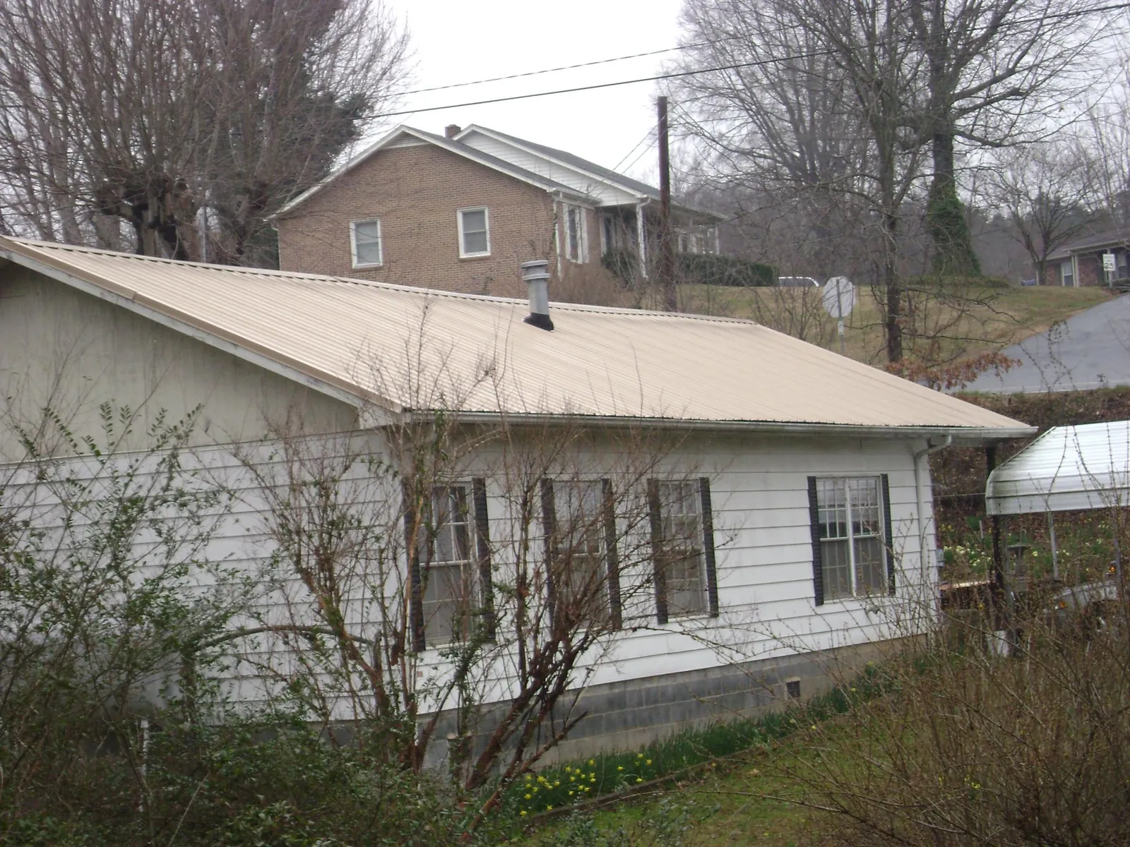 Tan metal roof on a white sided house set into a hillside — Commercial Roofing by Roofing Brothers in Ridgely