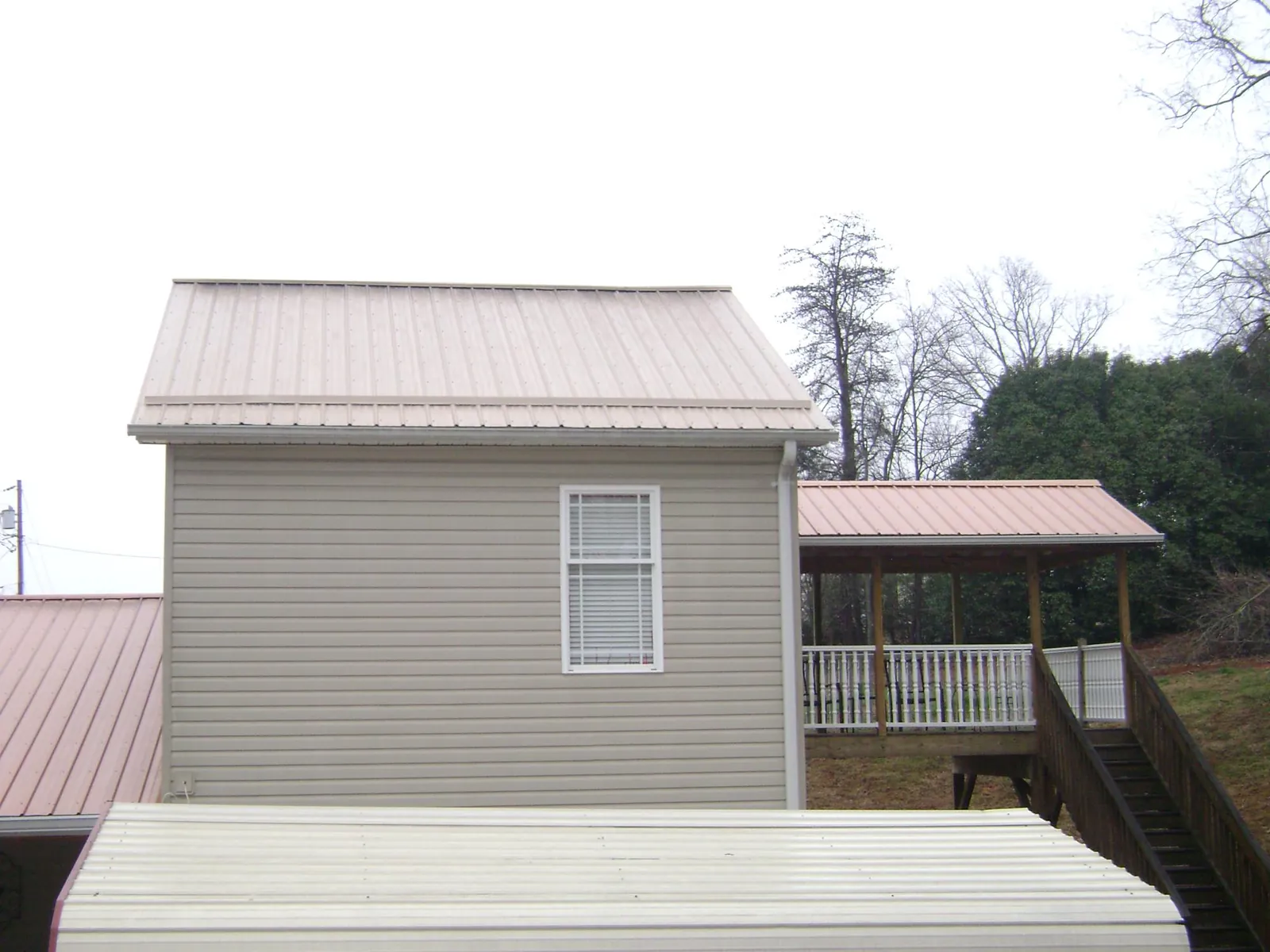 Tan metal roofs on a two story addition and attached porch, from a Roof Replacement job in Ridgely